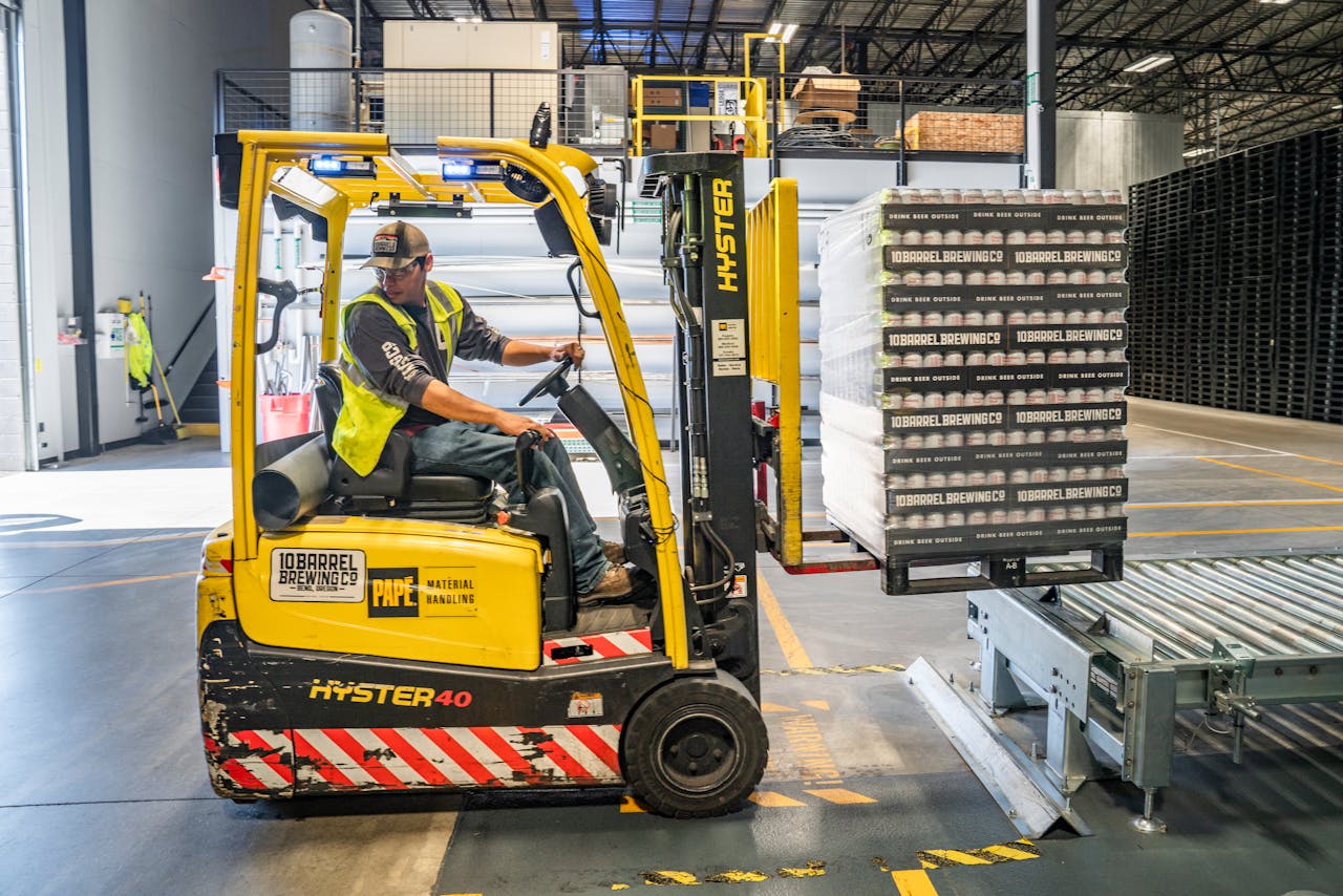 brand-03 A warehouse worker maneuvers a forklift to transport crates for brewing company storage.