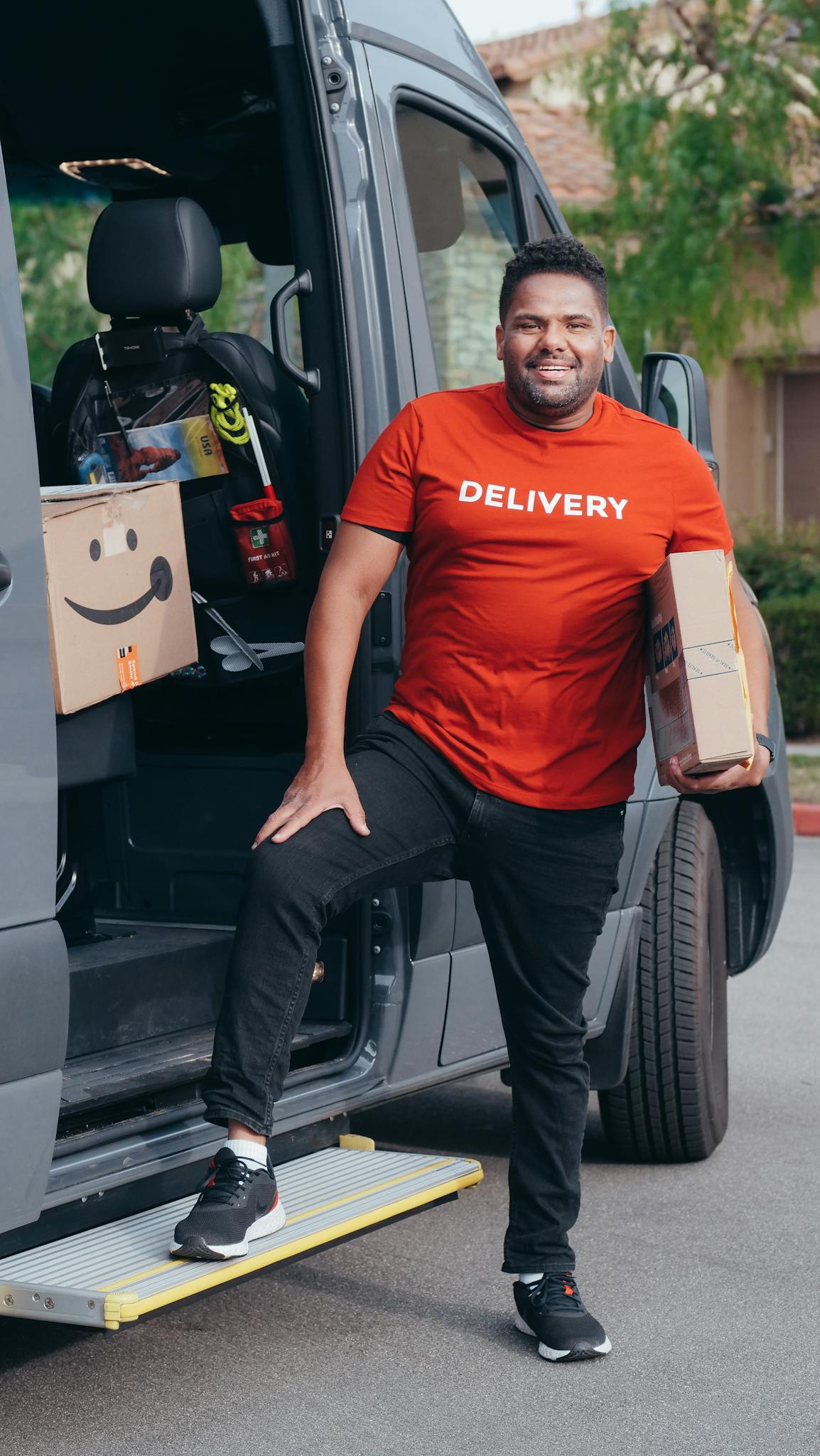 About A cheerful delivery man holding parcels next to his van during a workday.