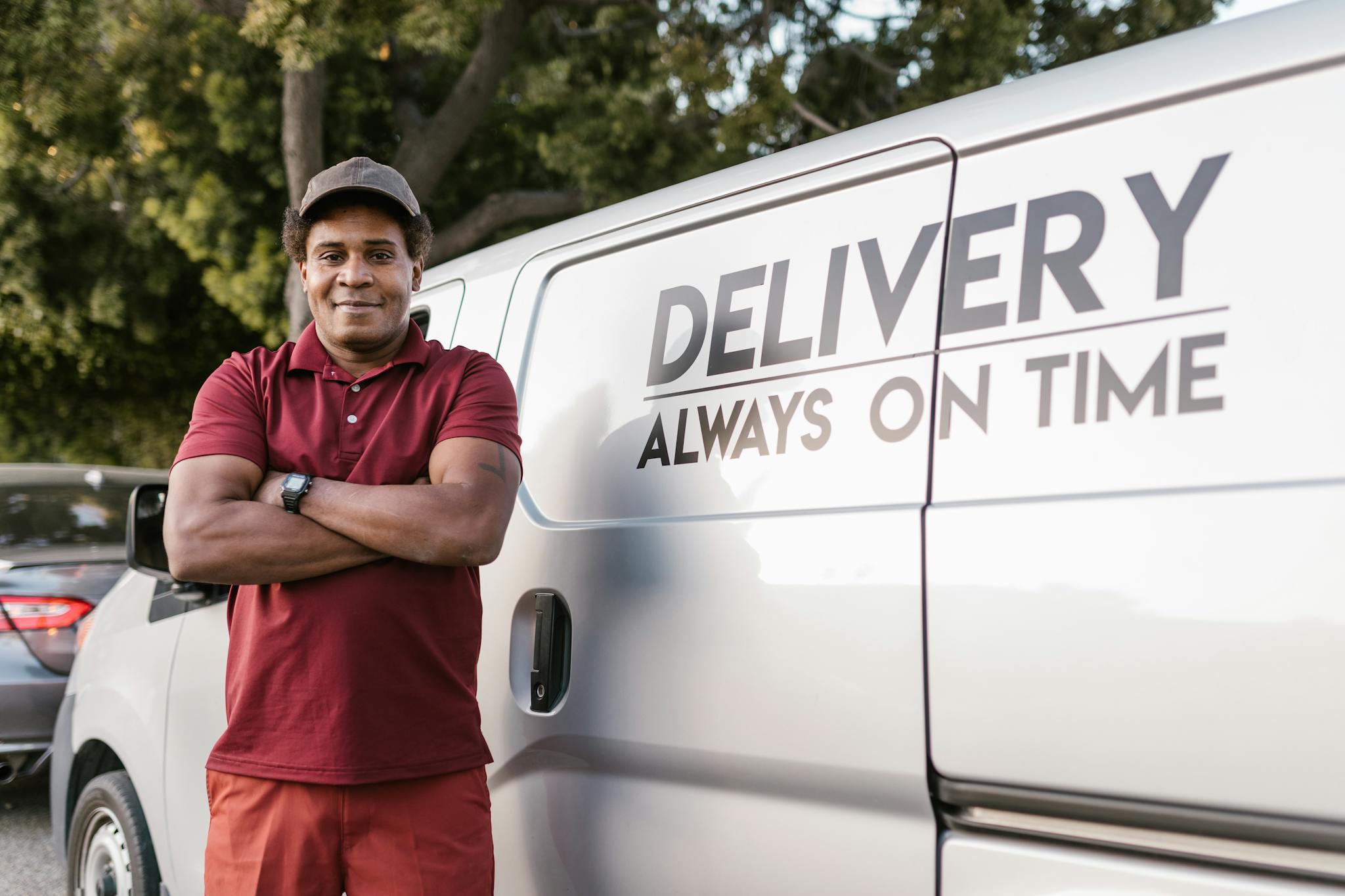 Home Delivery driver standing with arms crossed near a company van displaying a timely service slogan.