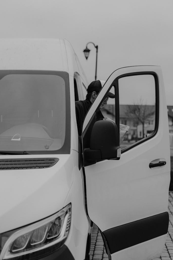 Services Monochrome image of a delivery driver stepping out of a van.