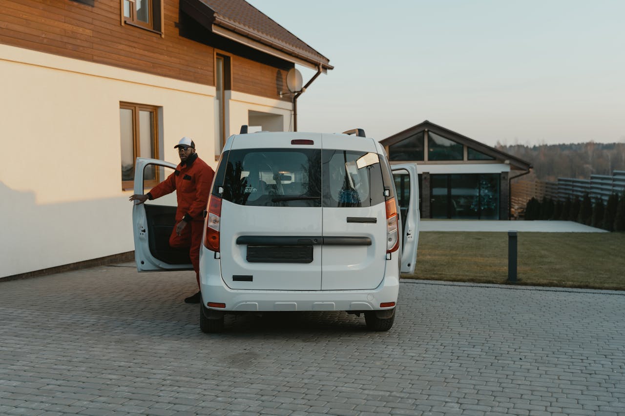 About A worker in uniform exits a white van parked in a residential driveway during daytime.