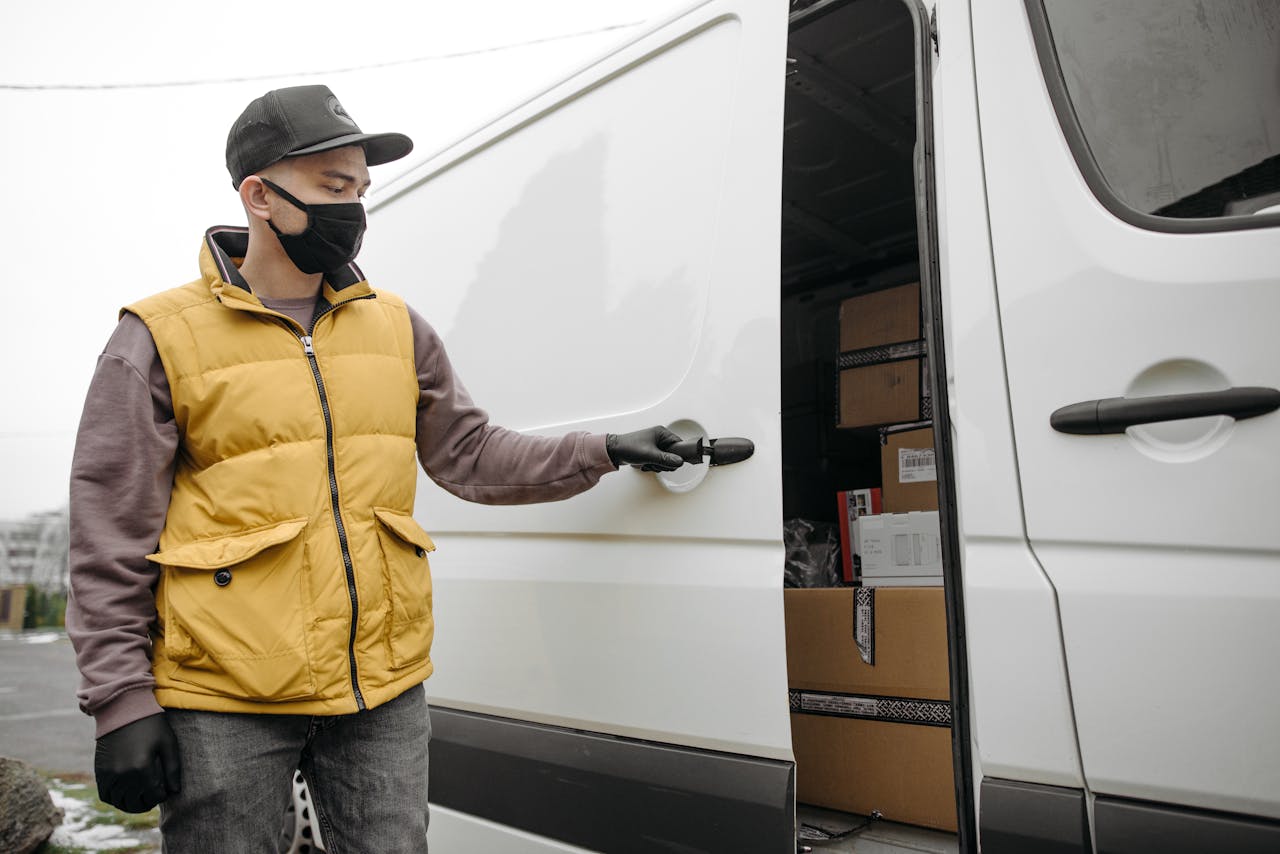 Delivery person opening a van full of packages, wearing a face mask and gloves.