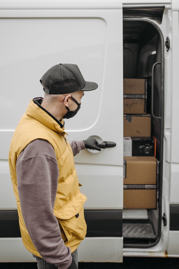 Services A courier in a yellow vest delivers packages from a van, emphasizing the new normal with safety protocols.