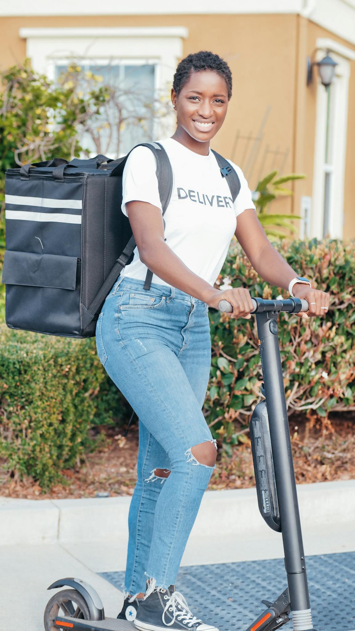 Smiling woman delivering packages using an electric scooter outdoors, representing modern delivery solutions.